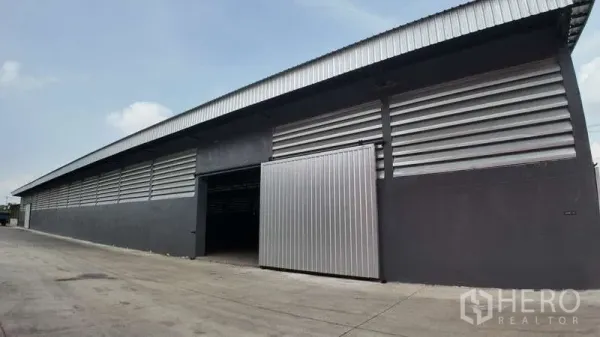 Warehouse for rent in Chachoengsao - Angled side view of the warehouse exterior showing a long facade, sliding metal door and wide driveway.