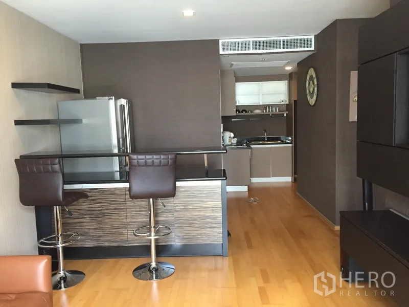 Condominium for rent or sale in Khlong Toei, Bangkok - Open-plan kitchen with breakfast bar, stools, and wood flooring in a modern Bangkok condo.
