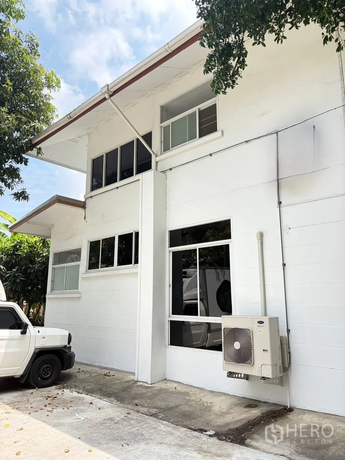 บ้านเดี่ยว for rent in Watthana, Bangkok - มุมใกล้ตัวบ้าน เห็นหน้าต่างบานใหญ่และคอมเพรสเซอร์แอร์ติดผนังข้างที่จอดรถ