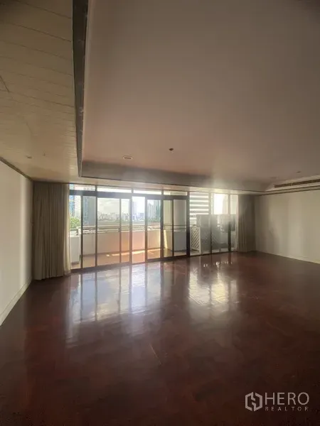 公寓 出租或出售在Watthana, Bangkok - 宽敞客厅，深色木地板，落地玻璃门通往阳台，眺望城市景观。
