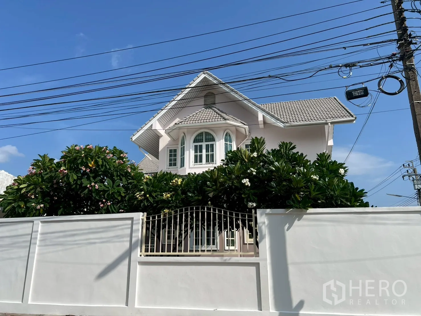独立式住宅 出售在Phra Khanong, Bangkok - 白色围墙后可见立面与繁茂的缅栀子树。