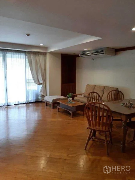 Apartment for rent in Watthana, Bangkok - Open-plan lounge with sofa, air conditioner and sliding glass doors to the balcony.