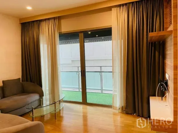 公寓 出租在Watthana, Bangkok - 客厅配沙发与玻璃茶几，推拉门通往铺草坪的阳台。