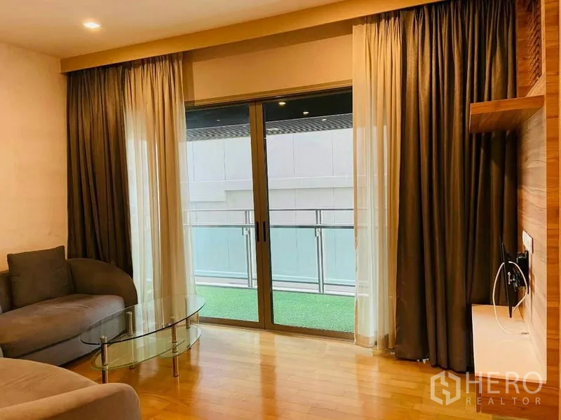 公寓 出租在Watthana, Bangkok - 客厅配沙发与玻璃茶几，推拉门通往铺草坪的阳台。