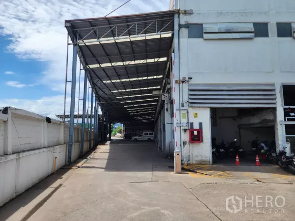 Factory for rent in Mueang Samut Sakhon, Samut Sakhon - Covered loading driveway along the factory side with a metal roof and roller shutters.