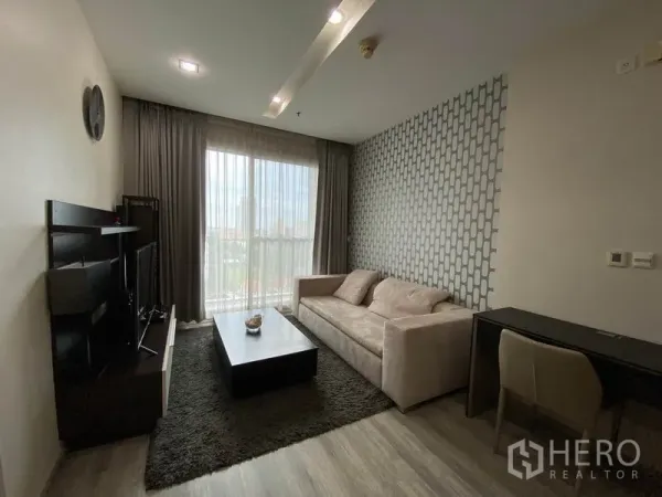 Condominium for rent or sale in Khlong Toei, Bangkok - Bright living room with sofa, TV unit, work desk and balcony window with city view.