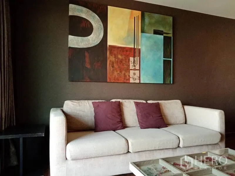 Condominium for rent in Sathon, Bangkok - Cream sofa with purple cushions beneath a large abstract painting on a dark accent wall.