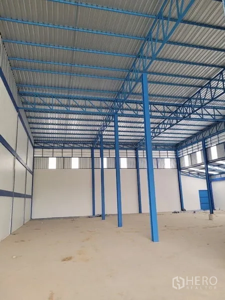 Factory for rent or sale in Khlong Luang, Pathum Thani - High-clearance warehouse interior featuring blue steel trusses and concrete floor.