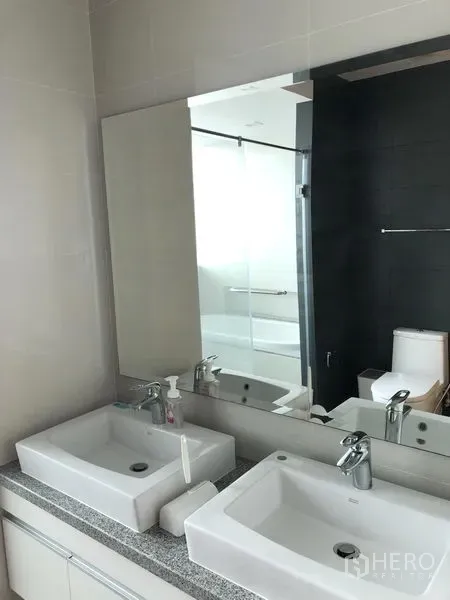 Condominium for rent in Khlong Toei, Bangkok - Modern bathroom with double vanity, large mirror, bathtub and toilet.