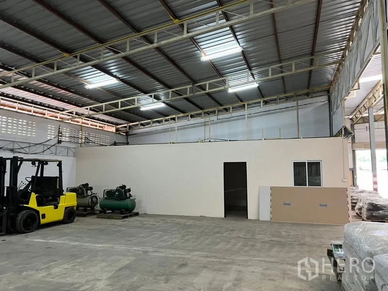 Warehouse for rent in Suan Luang, Bangkok - Warehouse floor with forklifts, air compressors and an internal office beneath a skylit steel structure.