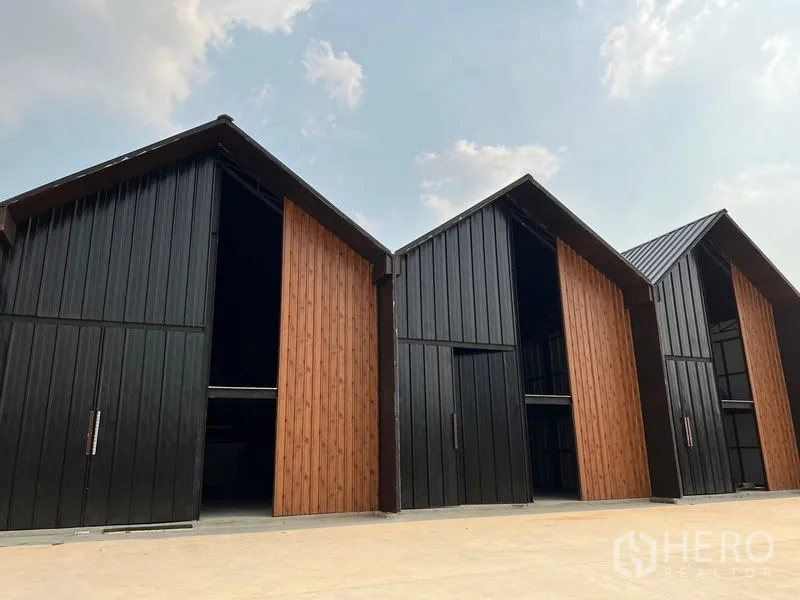 Warehouse for rent in Bueng Kum, Bangkok - Modern gabled warehouse units in Bueng Kum with black metal cladding, wood-accent doors and a wide paved loading area.