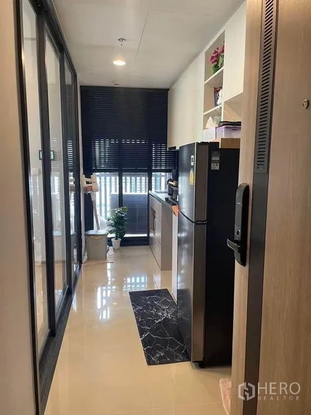 公寓 出租在Khlong Toei, Bangkok - 现代公寓的狭长一字型厨房，黑色台面、大冰箱与百叶窗。