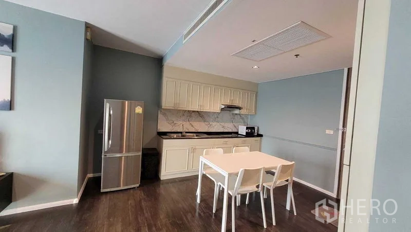 Condominium for rent in Khlong Toei, Bangkok - Open kitchen with cream cabinets, marble backsplash, stainless refrigerator and dining table.