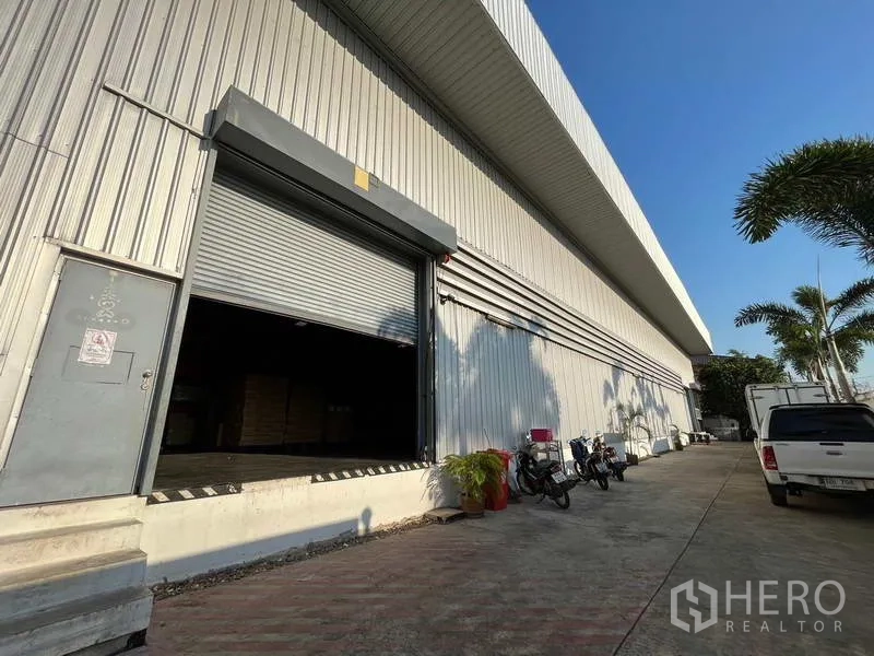 Warehouse for rent or sale in Nonthaburi - Raised loading dock with large rolling door and parking under a metal canopy.