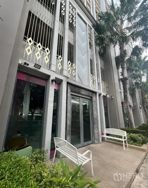 零售空间 出租在Khlong Toei, Bangkok - 现代零售店面，双层挑高立面、玻璃门、金色格栅，长椅与棕榈树步道，近BTS安努站。
