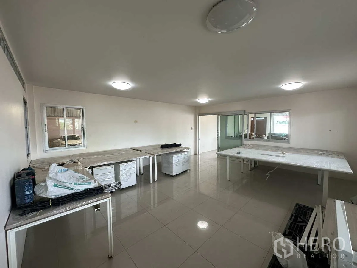 Factory for rent in Pathum Thani - Large office workspace with ceiling lights, multiple worktables and glass sliding doors.