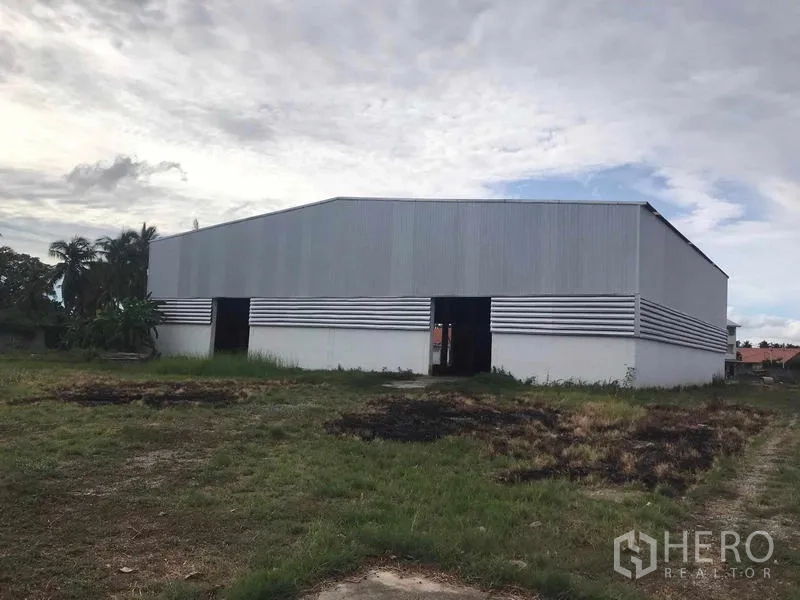 Warehouse for sale in Chon Buri - Rear view of steel-clad warehouse with striped siding and multiple access doors.