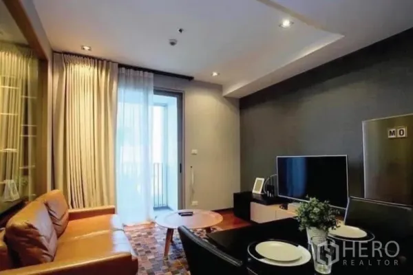 公寓 出售在Khlong Toei, Bangkok - 温馨客厅，棕色皮沙发、电视柜，落地窗通向阳台。