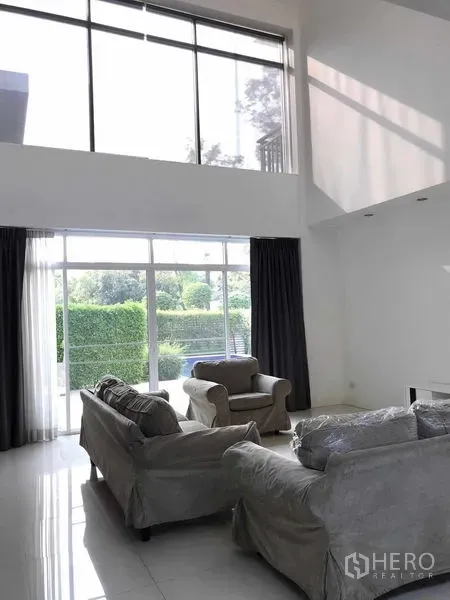 Detached House for sale in Wang Thonglang, Bangkok - Double-height living room with floor-to-ceiling windows and grey sofas opening to the garden