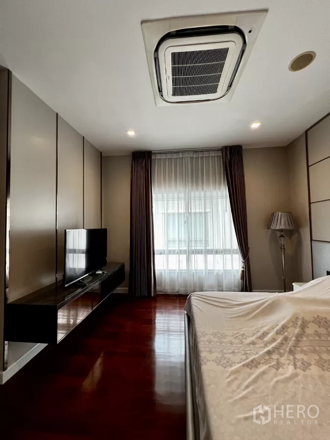 Detached House for rent or sale in Prawet, Bangkok - Primary bedroom with polished wood flooring, wall-mounted TV and cassette air conditioning.