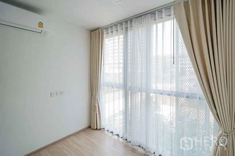 公寓 出租在Watthana, Bangkok - 明亮转角空间，整面落地窗与米色窗帘。