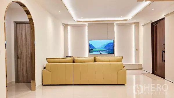 Detached House for rent or sale in Prawet, Bangkok - Minimalist lounge view with arch doorway, large windows and a TV feature wall behind a beige sofa.