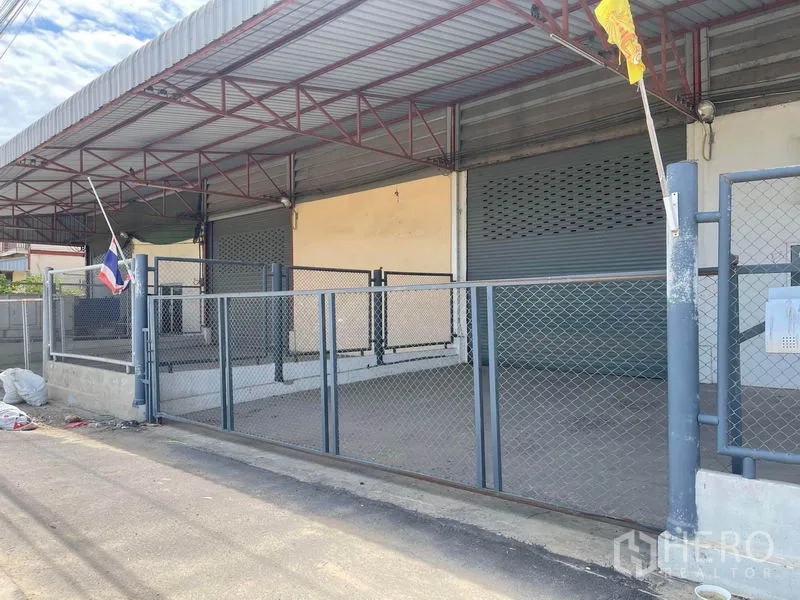 Factory for rent in Lat Lum Kaeo, Pathum Thani - Angled view of raised loading dock under a metal roof with two roller shutters and gated frontage.