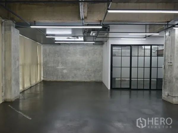Office Space for rent in Khlong Toei, Bangkok - Office interior with concrete walls, ducted ceiling lights, vertical blinds and a glass-framed meeting room.