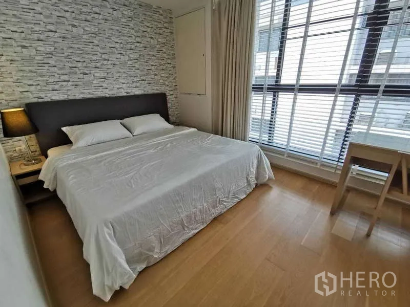 公寓 出租或出售在Watthana, Bangkok - 卧室设大床与石纹装饰墙，落地窗和书桌