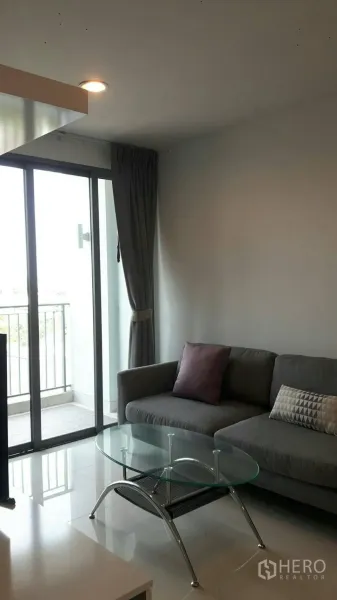 Condominium for rent in Phaya Thai, Bangkok - Cozy sofa corner with a glass coffee table and floor-to-ceiling balcony doors offering city views.