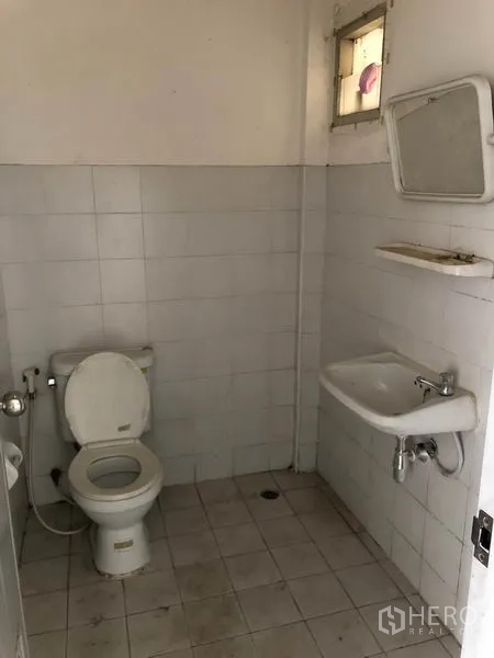 Factory for rent in Nonthaburi - Simple tiled restroom with a toilet, sink and small window.