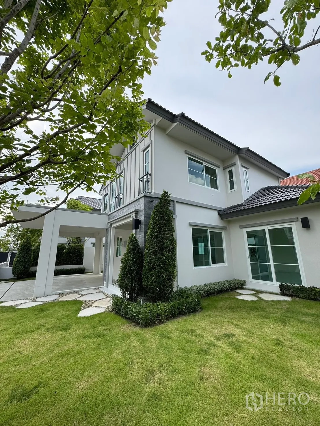 Detached House for rent in Bang Phli, Samut Prakan - Corner exterior of a two-storey home with lush lawn and mature trees.