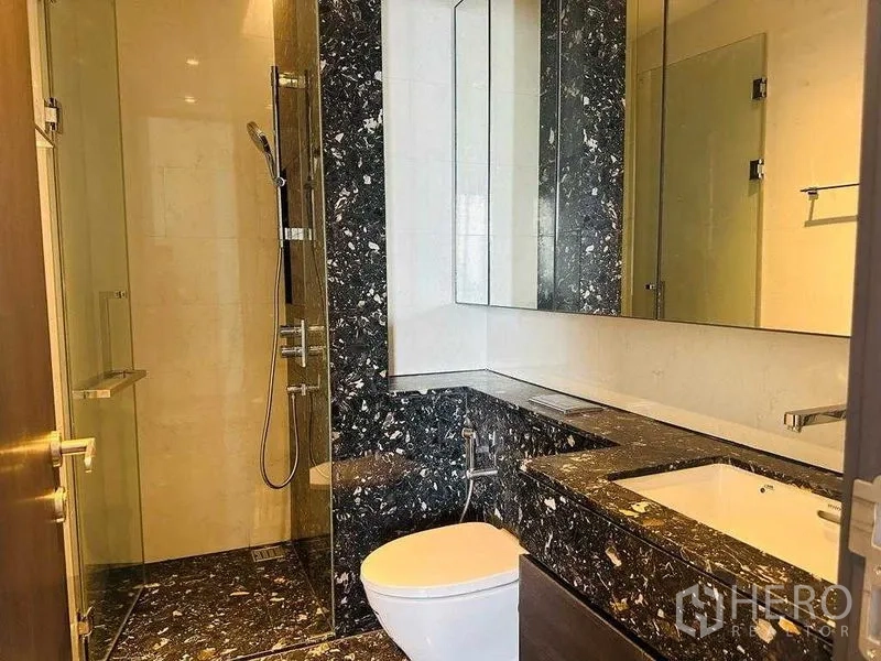Condominium for rent in Khlong Toei, Bangkok - Second bathroom with glass shower, black marble countertop, and large mirror.