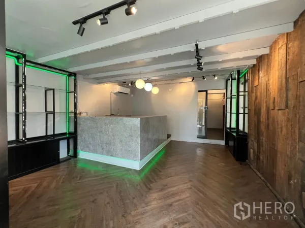 Retail Space for rent in Watthana, Bangkok - Open-plan sales space with green LED shelving, a wood accent wall, herringbone flooring and ceiling spotlights.