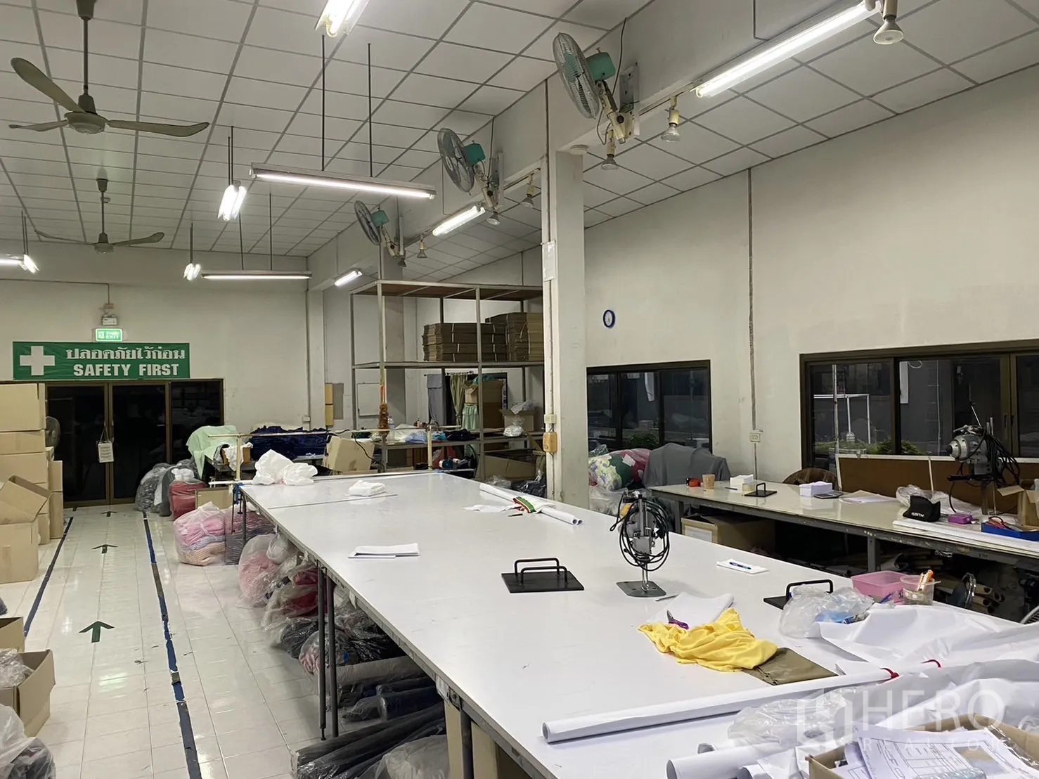 Factory for rent in Prawet, Bangkok - Bright production hall with high ceiling, ceiling fans, fluorescent lighting and long work tables.