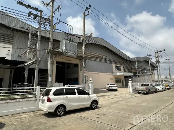Factory for rent in Samut Prakan - Side view of the factory exterior along an industrial street with transformer, high-clearance loading bay and overhead power lines.
