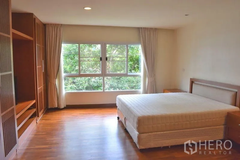 Apartment for rent in Sathon, Bangkok - Bedroom with king‑size bed, floor‑to‑ceiling windows and wood floors.