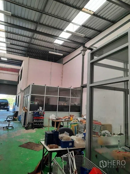 Warehouse for sale in Samut Prakan - Interior view toward the entrance showing partitioned rooms, equipment and high roof.