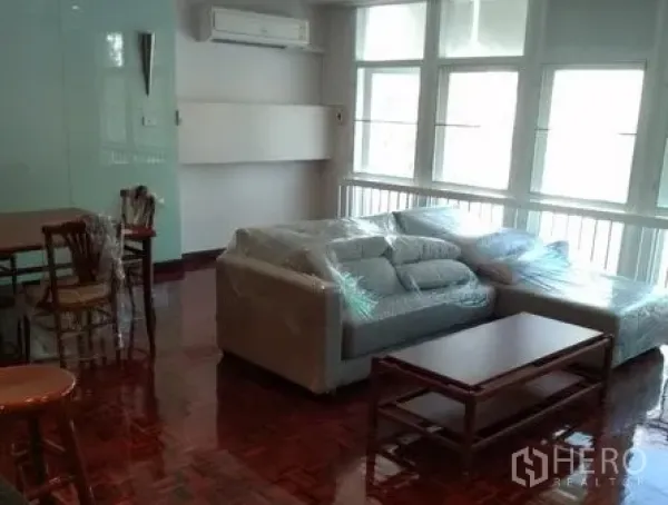 Apartment for rent in Pathum Wan, Bangkok - Bright living room in Lumphini apartment with large windows, parquet floors, grey sofa and coffee table near BTS Phloen Chit.