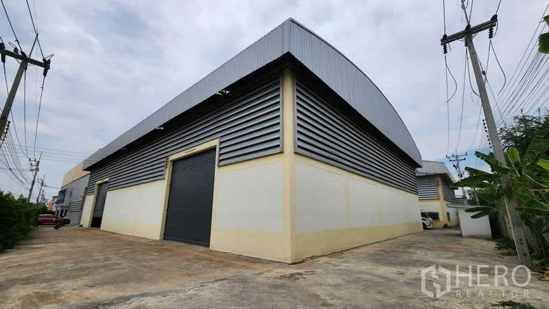 โรงงาน ให้เช่าในBan Phaeo, Samut Sakhon - ด้านนอกโรงงานกรุเมทัลชีท พร้อมประตูม้วนขนาดใหญ่ และทางวิ่งกว้างสำหรับรถคอนเทนเนอร์