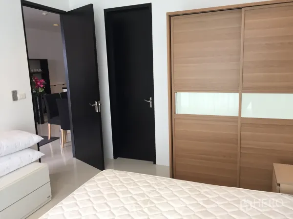 公寓 出租在Ratchathewi, Bangkok - 卧室内推拉木质衣柜，亮面地砖与通往起居区的门。