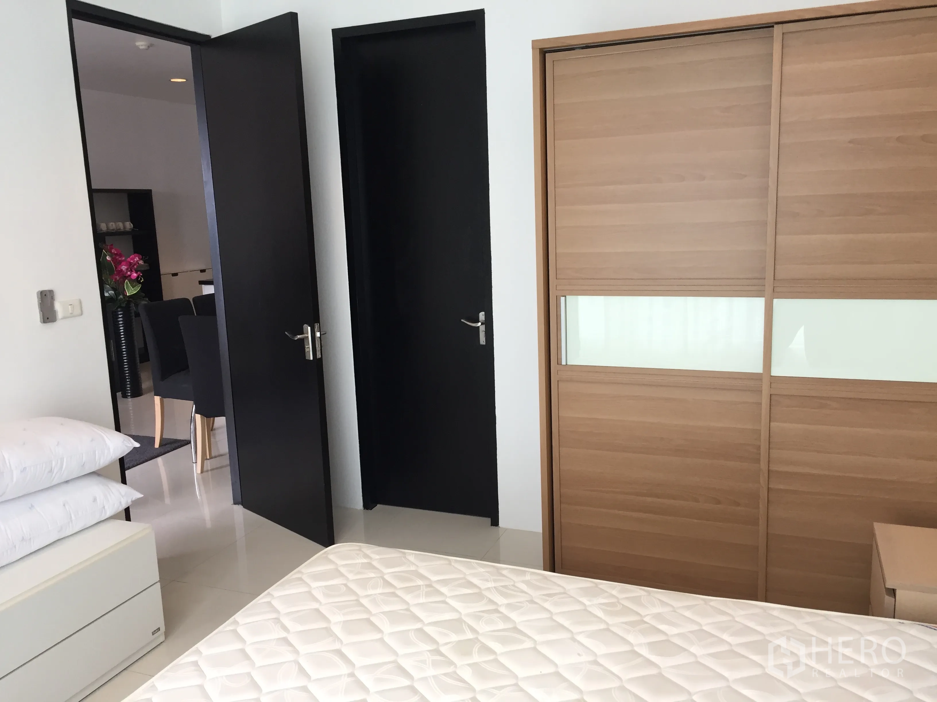 公寓 出租在Ratchathewi, Bangkok - 卧室内推拉木质衣柜，亮面地砖与通往起居区的门。