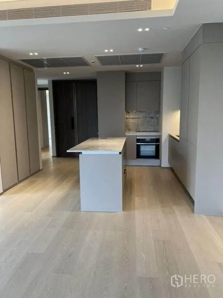 Condominium for rent in Pathum Wan, Bangkok - Kitchen island with stone countertop facing tall cabinets and built-in appliances.