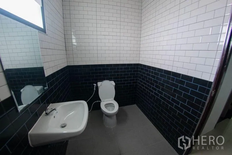Warehouse for sale in Krathum Baen, Samut Sakhon - Clean restroom with white subway tiles and dark wainscot, sink and toilet.
