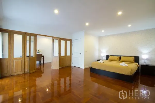 Apartment for rent in Watthana, Bangkok - Spacious bedroom with king bed, built-in wardrobes with glass panels, recessed lighting, and wood flooring.