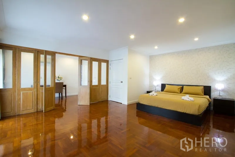Apartment for rent in Watthana, Bangkok - Spacious bedroom with king bed, built-in wardrobes with glass panels, recessed lighting, and wood flooring.