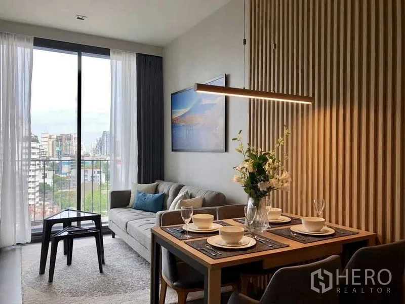 公寓 出租在Watthana, Bangkok - 客厅带推拉门通阳台，可见城市景观，四人餐桌靠木质格栅墙。