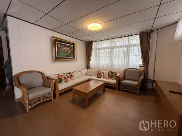 Detached House for rent in Phra Khanong, Bangkok - Cozy living room with rattan armchairs, L-shaped sofa, wooden table and curtained windows.