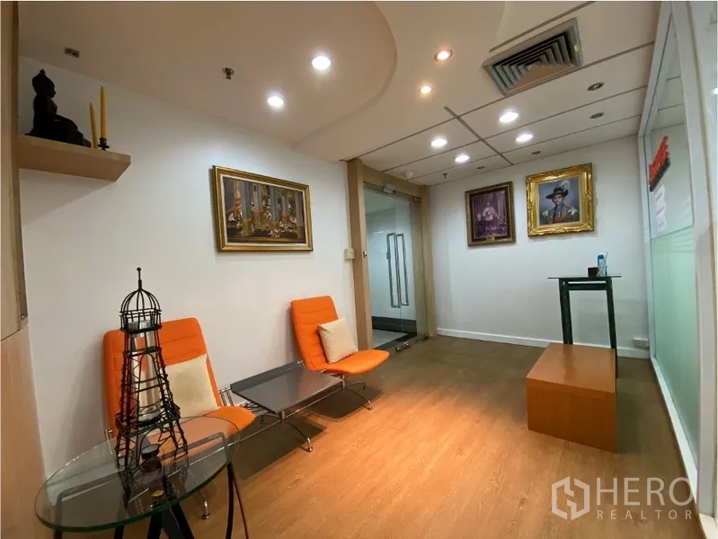 办公空间 出租在Khlong Toei, Bangkok - 接待休息区，橙色座椅、玻璃小桌、墙面装饰画与筒灯。