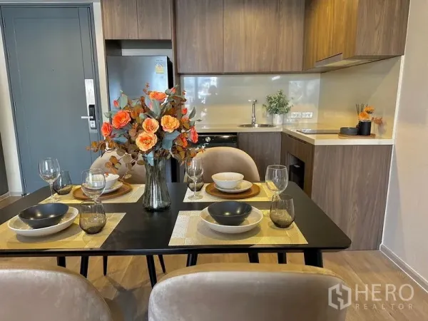 Condominium for rent in Pathum Wan, Bangkok - Dining table set for four next to a wood-finished kitchenette with upper cabinets.